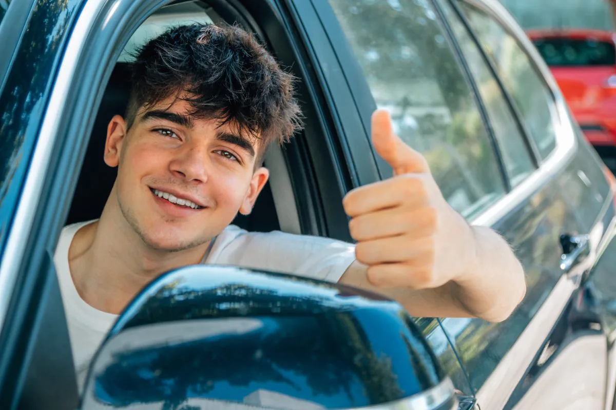 Tevreden jongeman toont thumbs up vanuit auto na advies over auto theorie examen in 1 dag